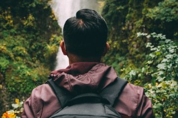 man looking up the bridge near the waterfalls